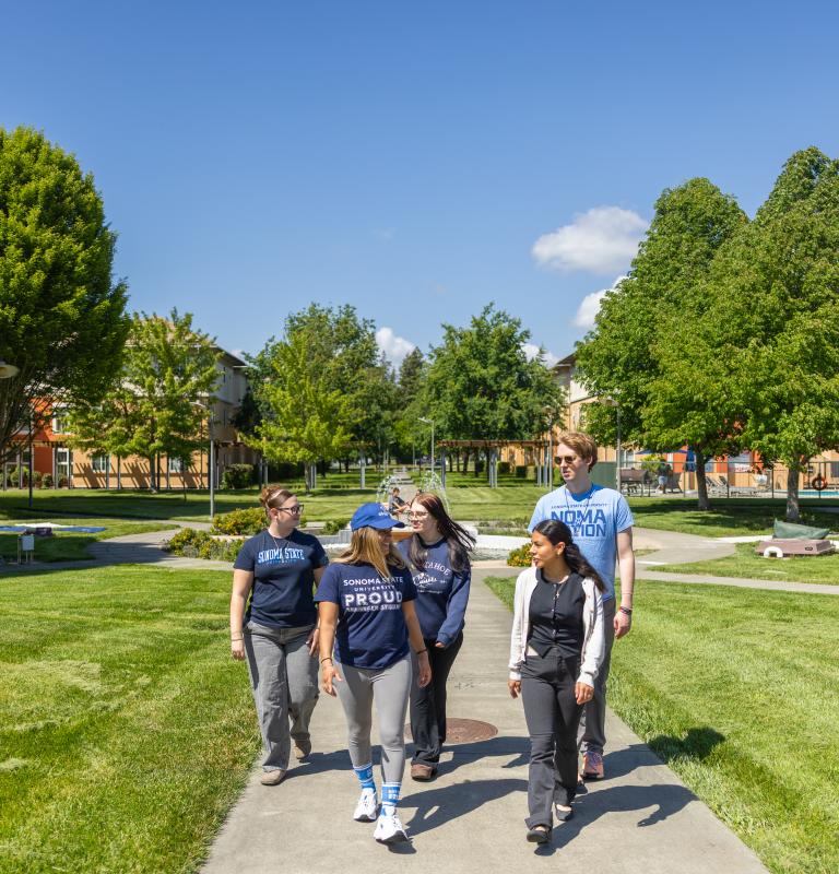 Five students walking through Beaujolais housing village with pool behind them on the right and housing buildigns behind them on the left