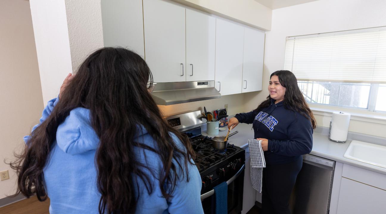 Two studnents in a kitchen cooking at the stove and talking