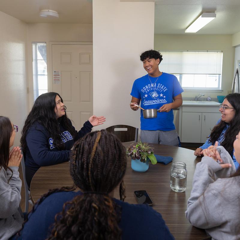 Six students sitting around a kitchen table talking