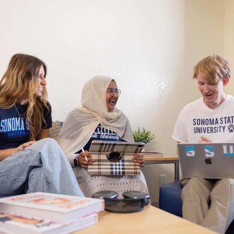 Three students sitting talking and on a computer