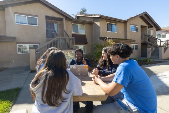 Five students sitting outside Sauvignon Village looking at a computer and talking