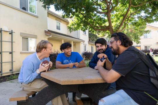 Group of guys hanging out outside at a table and talking