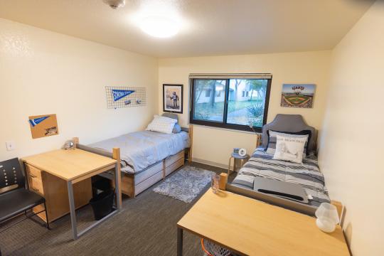 Dorm room with two beds and a desk