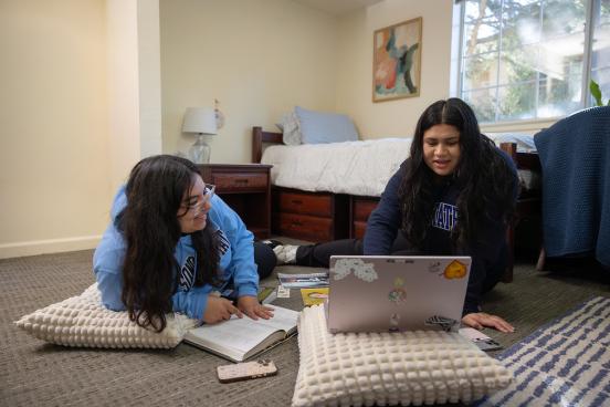Two students sitting on floor in dorm room looking at a computer and studying