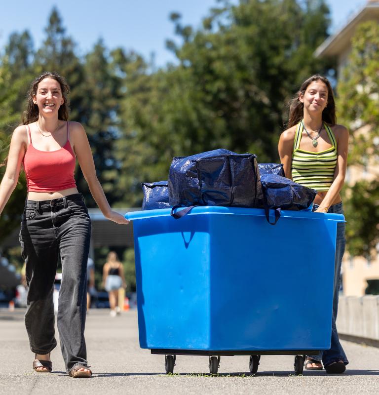 Two students with a moving cart and blue bags