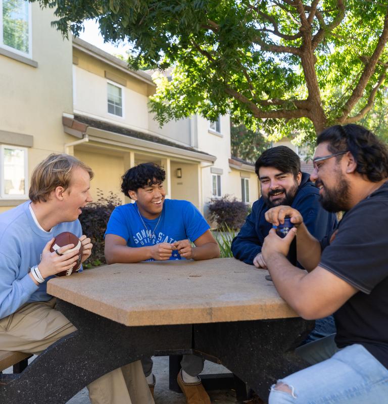 Group of guys hanging out outside at a table and talking