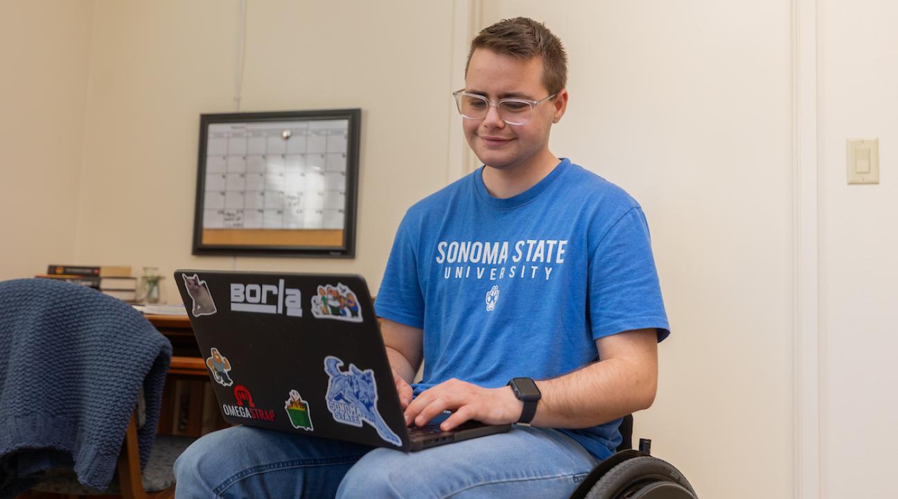 Student sitting with computer on their laptop with desk in background
