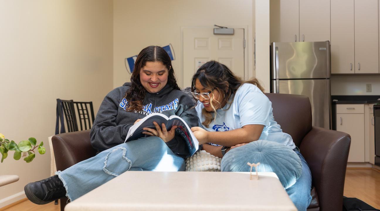 Two students looking at a book and sitting in the living room