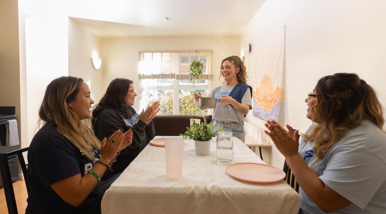 Three students at a dining room tabling with one student serving dinner