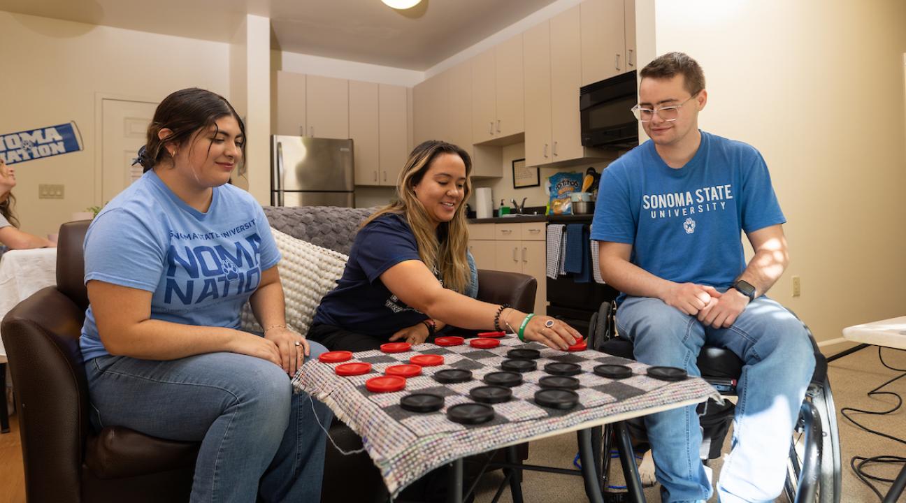 Three students sitting playing chess in a living room