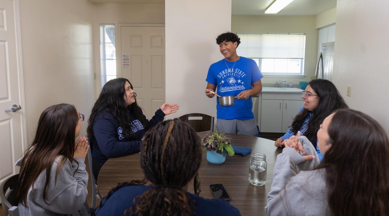 Six students sitting around a kitchen table talking