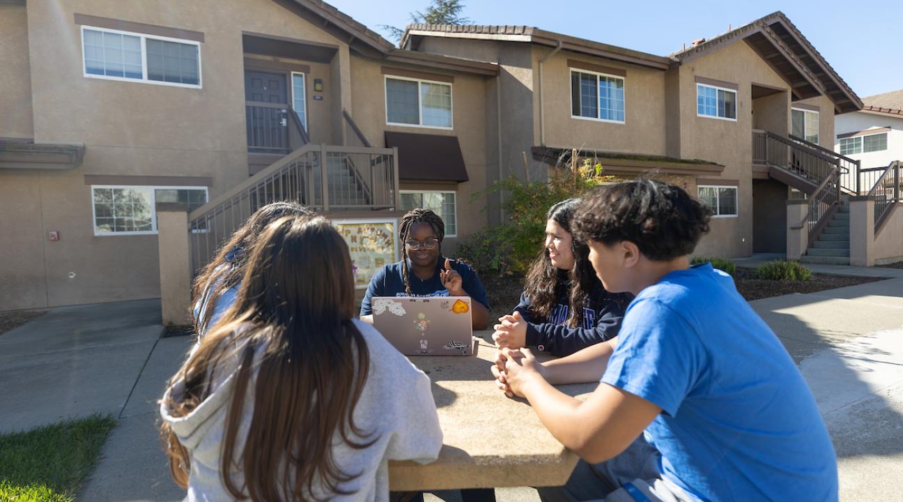 Five students sitting outside Sauvignon Village looking at a computer and talking