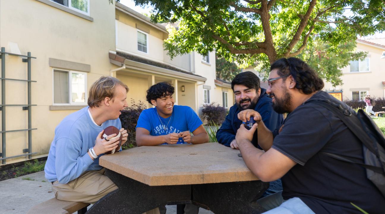 Group of guys hanging out outside at a table and talking