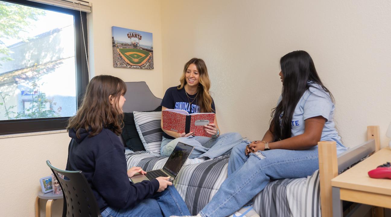 Three students sitting on a bed socializing