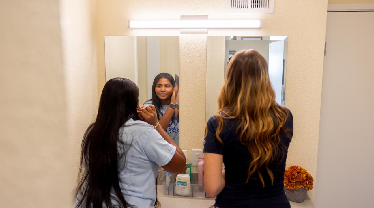 Two students looking into bathroom mirror getting ready