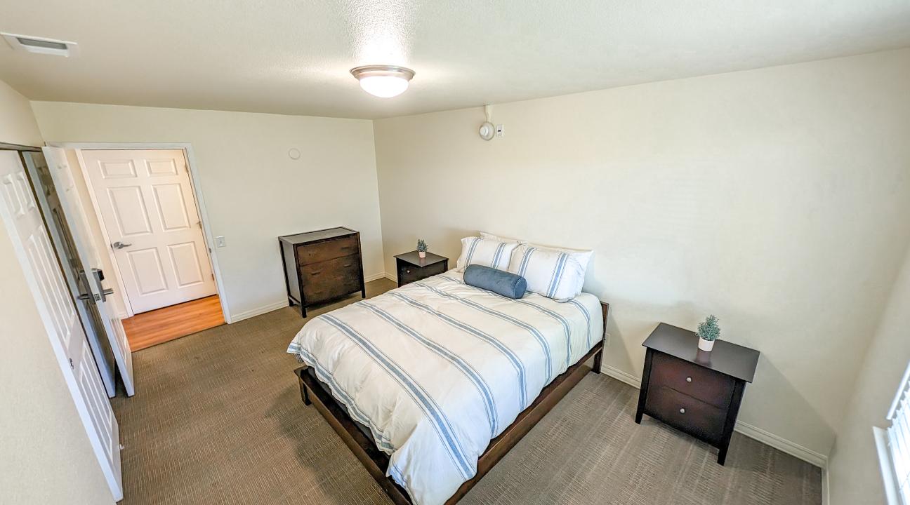 A spacious bedroom furnished with a queen sized bed, dresser, and two nightstands