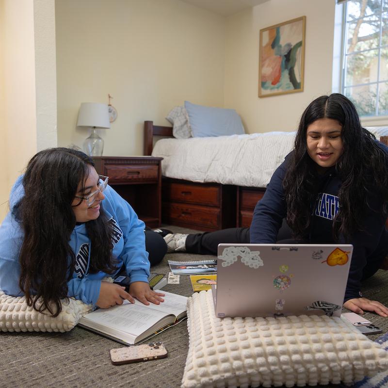Two people sitting on the floor studying in a dorm room
