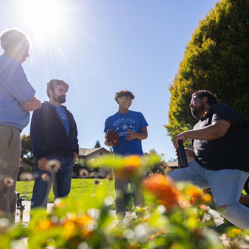 Four students hanging out outside and standing and talking