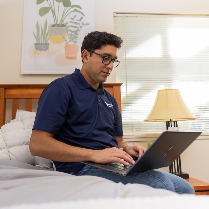 Student sitting on bed with laptop in lap