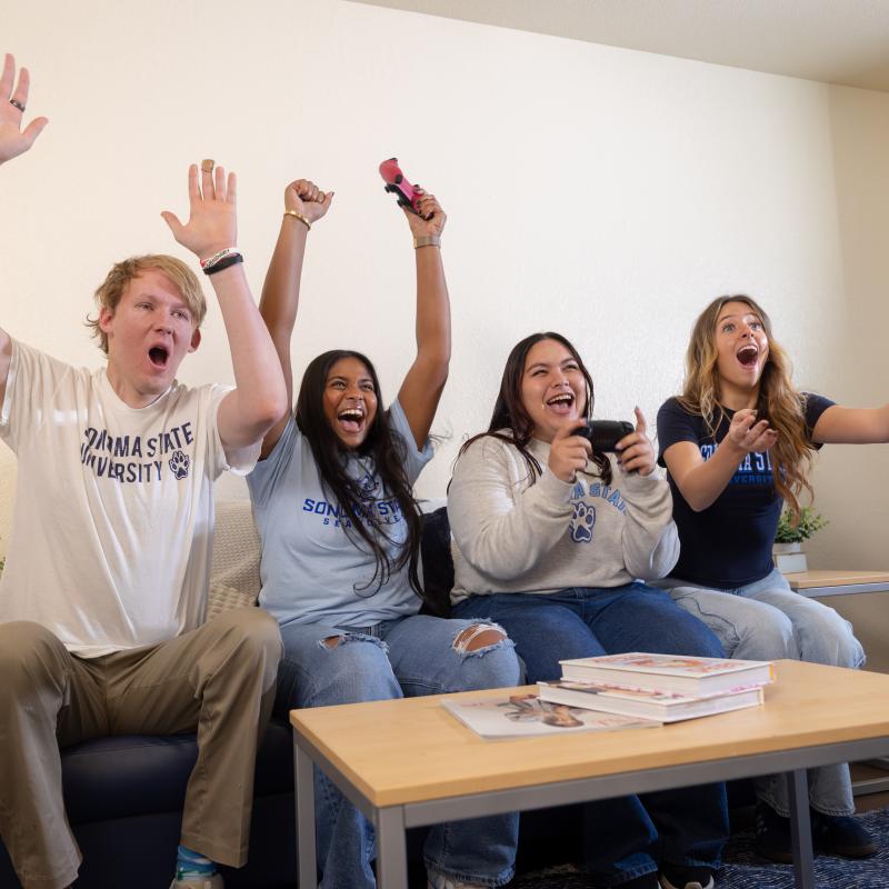 Students sitting on couch cheering and playing video games
