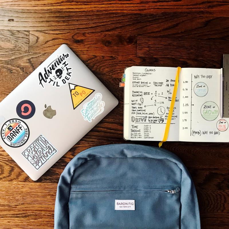 Computer and notebook and backpack on a wood surface