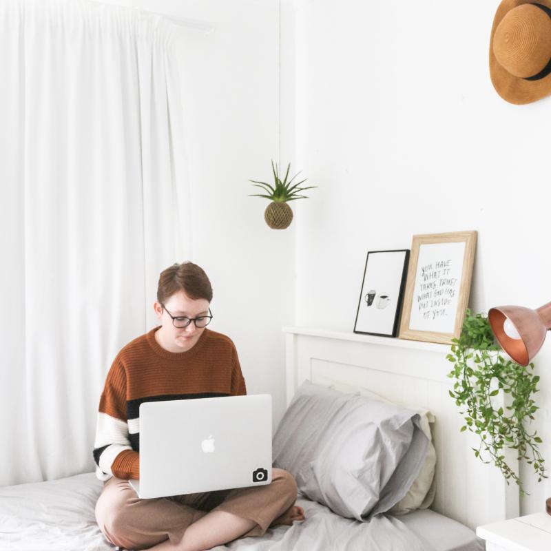 Student on computer sitting on a bed