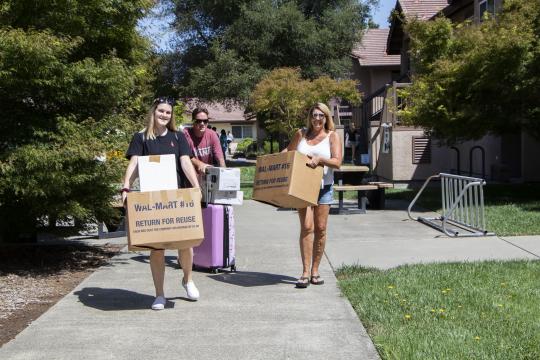 students walking onto campus carrying bags and boxes