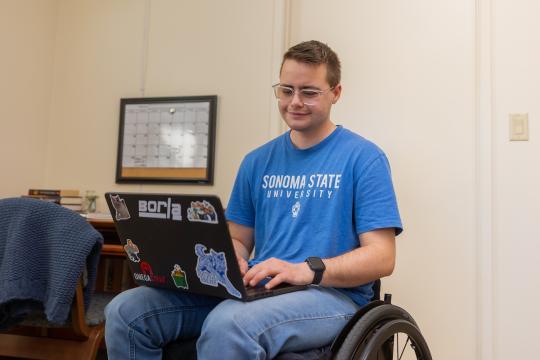 Student sitting with computer on their laptop with desk in background