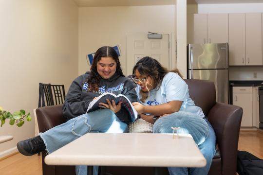Two students looking at a book and sitting in the living room