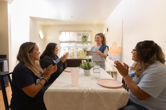 Three students at a dining room tabling with one student serving dinner