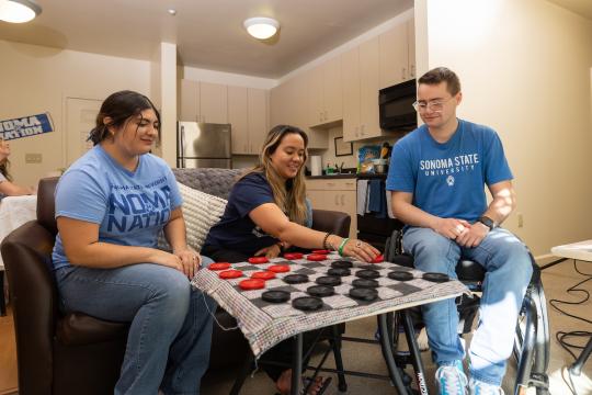 Three students sitting playing chess in a living room