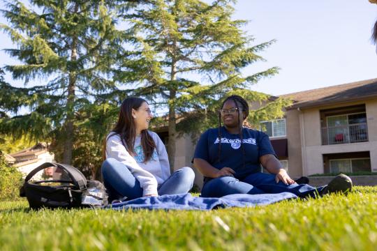 Two students sitting on the lawn socializing