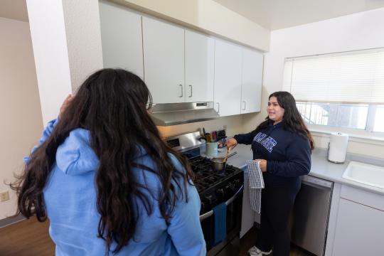 Two studnents in a kitchen cooking at the stove and talking