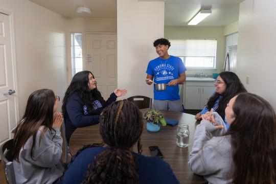 Six students sitting around a kitchen table talking