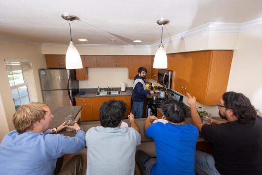 Group of students sitting at kitchen counter while a student cooks at the stove