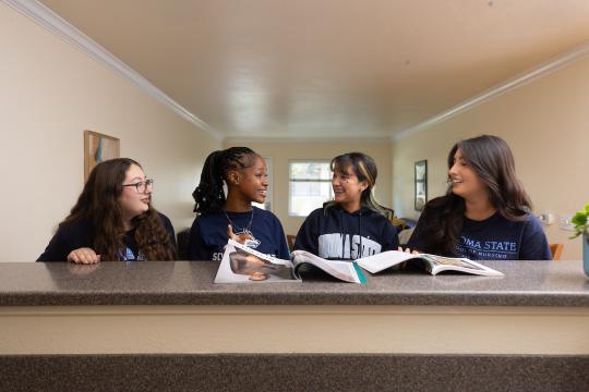Four students sitting at kitchen counter socializing
