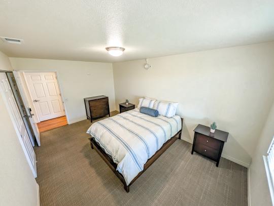 A spacious bedroom furnished with a queen sized bed, dresser, and two nightstands
