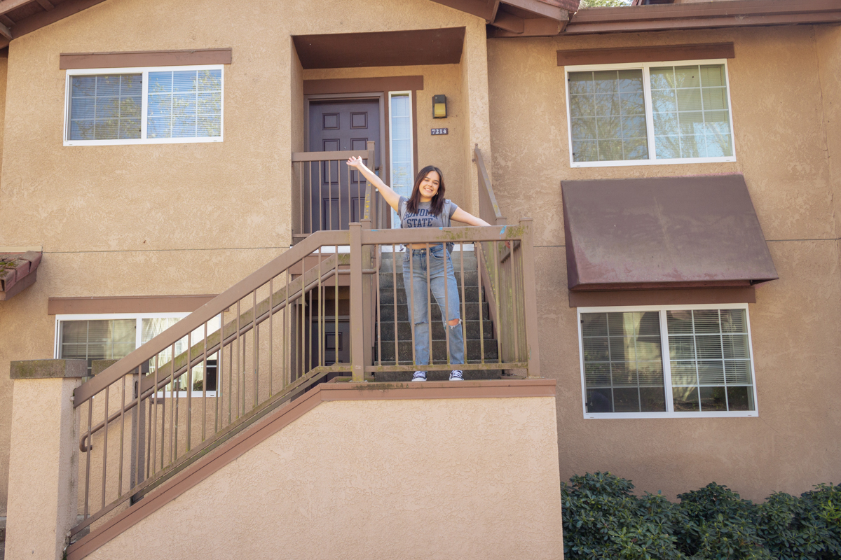 Student standing in front of Sauvignon building with hands up in the air